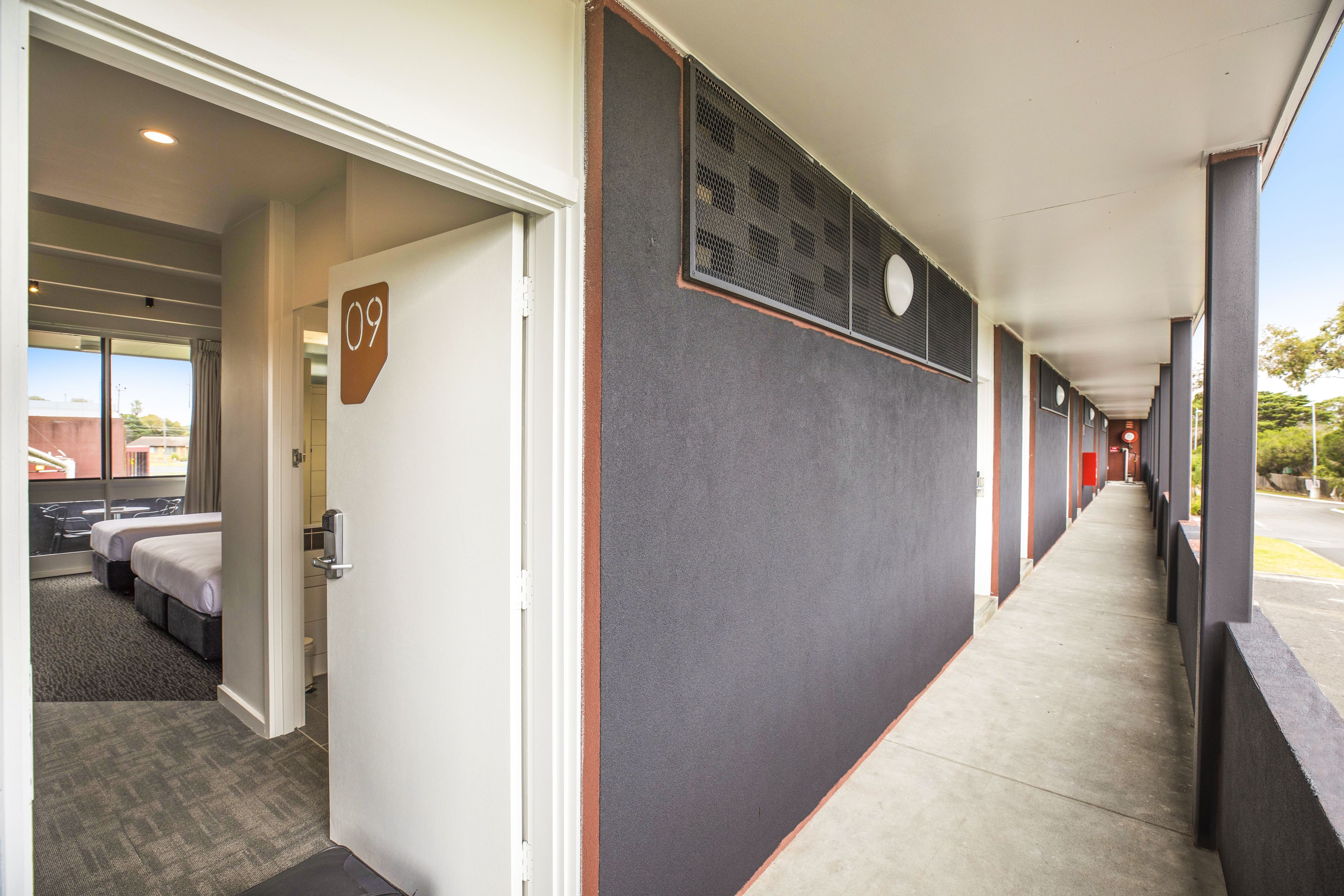 A hotel corridor with a number '09' sign, a bed, and a window with a view of the outside.