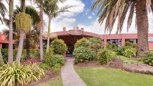 A hotel entrance with a pathway leading to the building, surrounded by palm trees and various plants.