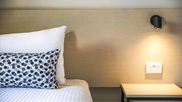 A neatly made bed with a striped bedspread and patterned pillows, a wall-mounted light, and a power outlet on a bedside table.