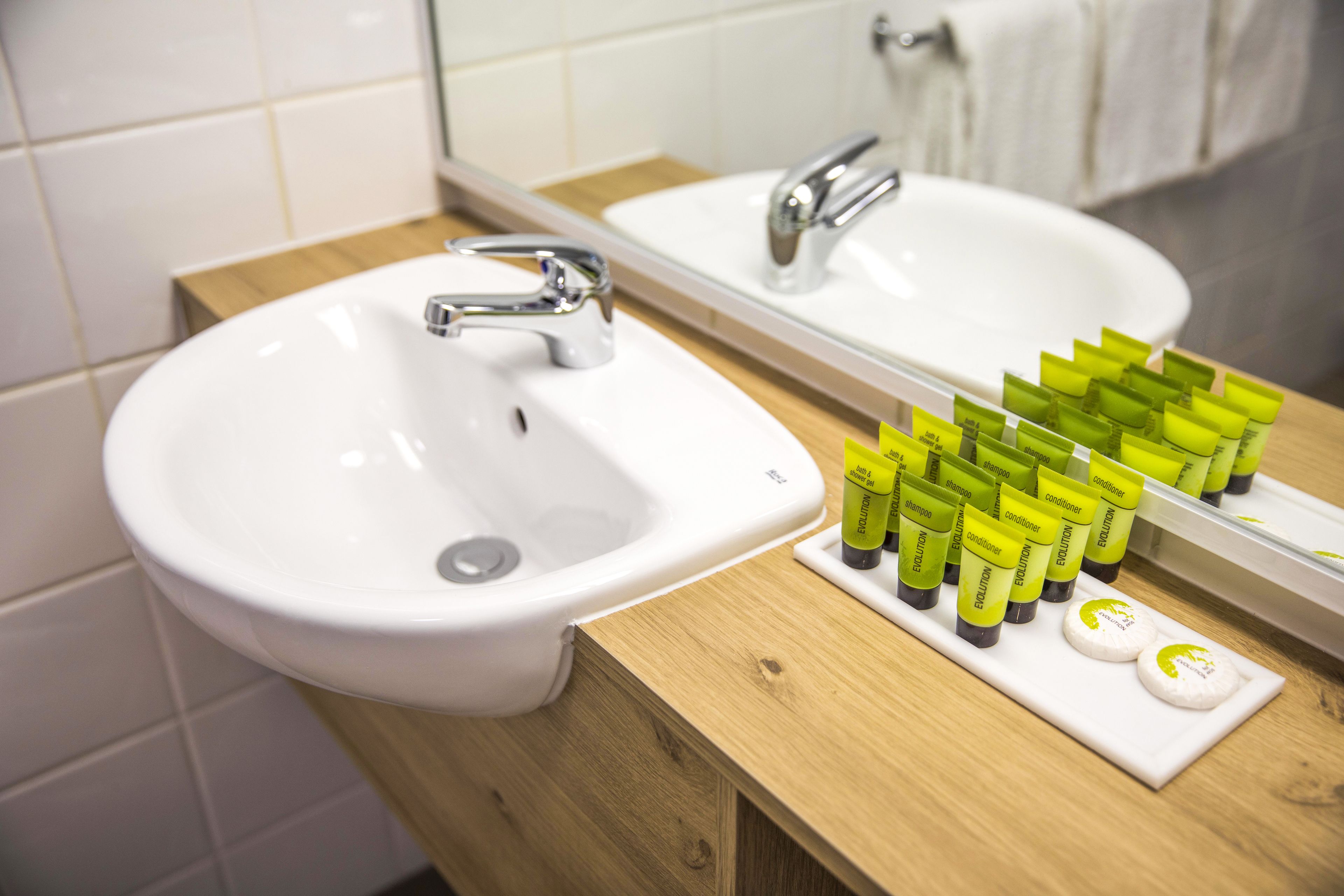 A bathroom with a white sink, a mirror, and a wooden vanity. There are several green and white toiletries on the vanity.