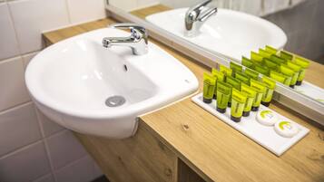 A bathroom with a white sink, a mirror, and a wooden vanity. There are several green and white toiletries on the vanity.