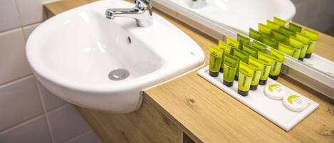 A bathroom with a white sink, a mirror, and a wooden vanity. There are several green and white toiletries on the vanity.