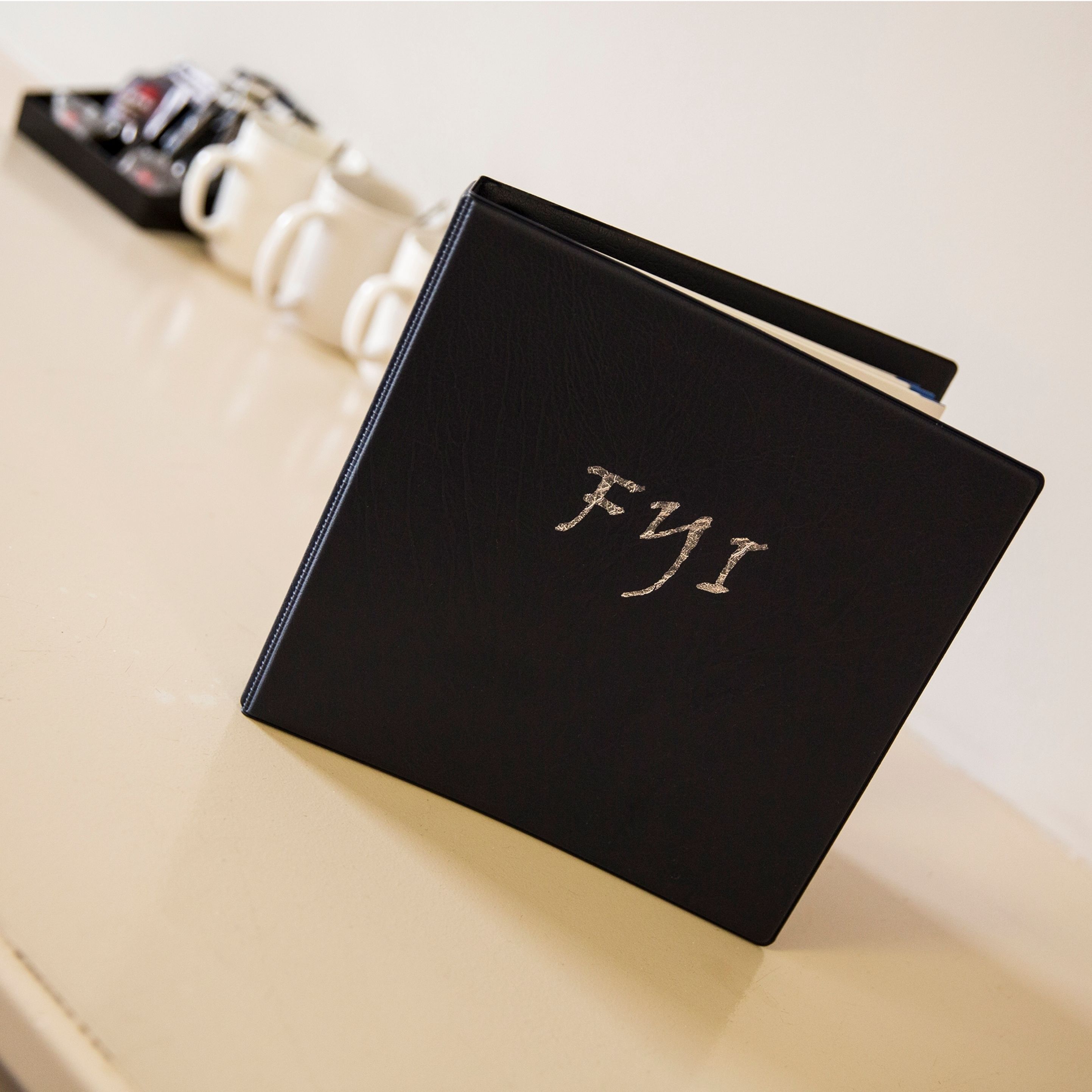 A black folder with the letters "FYI" embossed on it, placed on a beige surface.