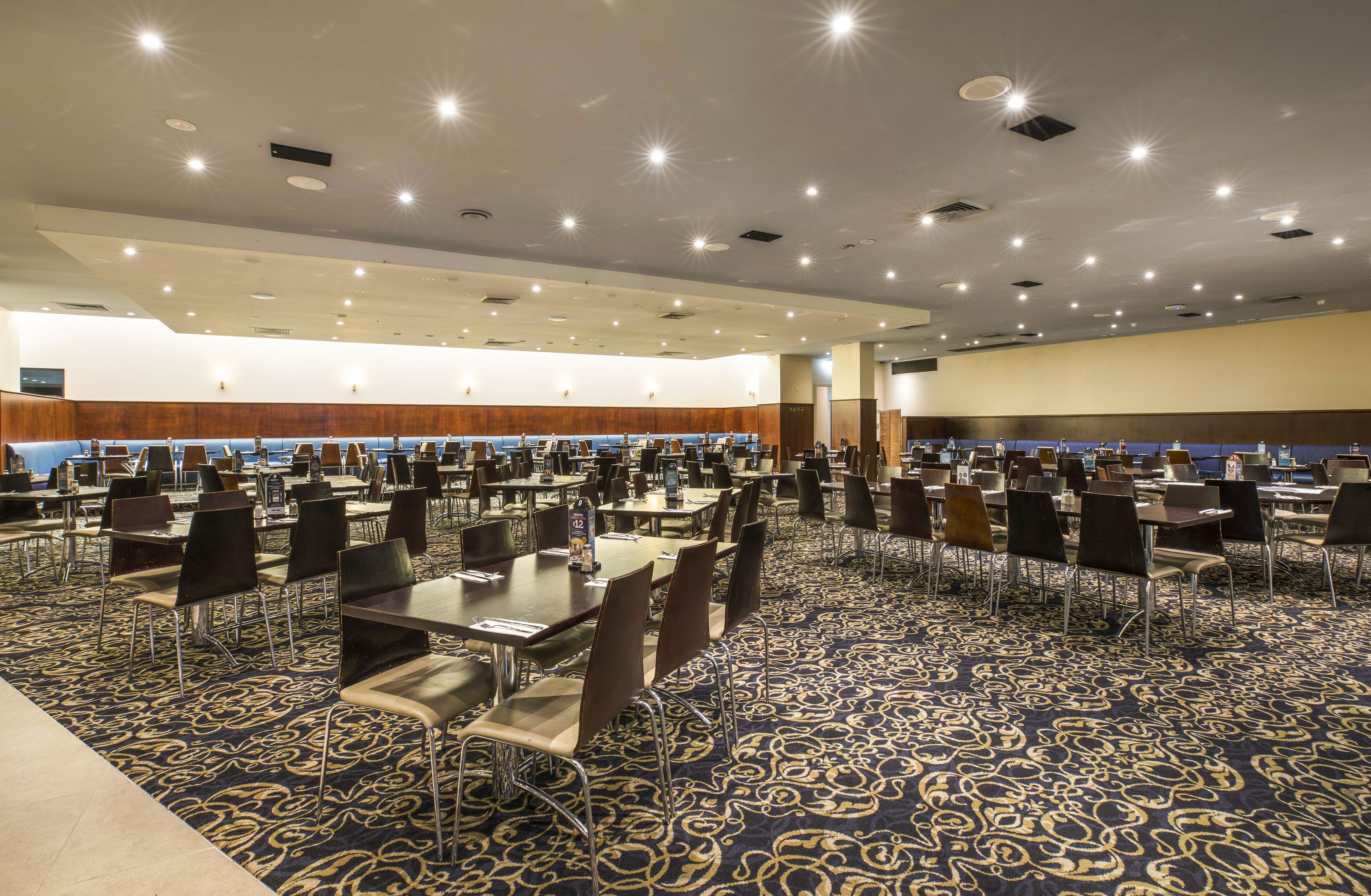 Een ruime congreszaal met meerdere tafels en stoelen, een vloerbedekking en ingebouwde verlichting.