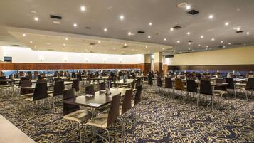 Een ruime congreszaal met meerdere tafels en stoelen, een vloerbedekking en ingebouwde verlichting.