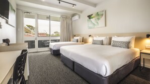 A hotel room with two beds, a desk, and a large window with a view.