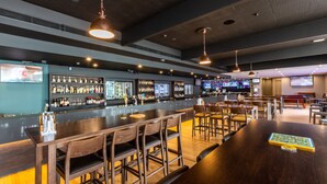 Un bar moderno con varias zonas de estar, una barra bien surtida e iluminación colgante.