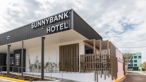 Hotel Sunnybank con fachada moderna, un acceso cubierto y un cartel que indica servicios como comida, bebida y entretenimiento.