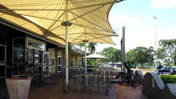 An outdoor seating area with umbrellas, potted plants, and a view of the street.