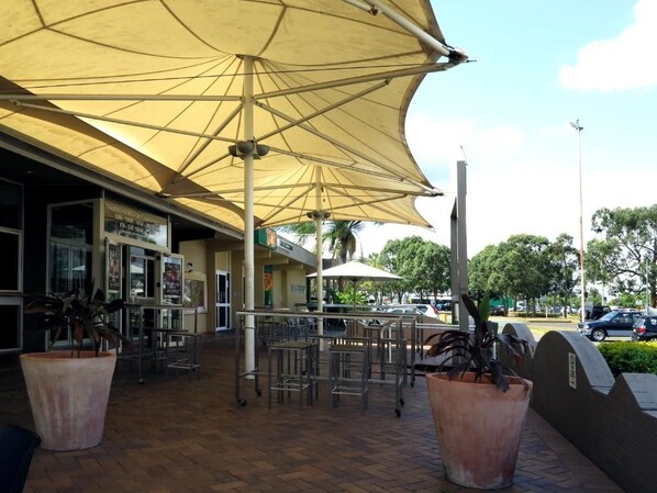 An outdoor seating area with umbrellas, potted plants, and a view of the street.