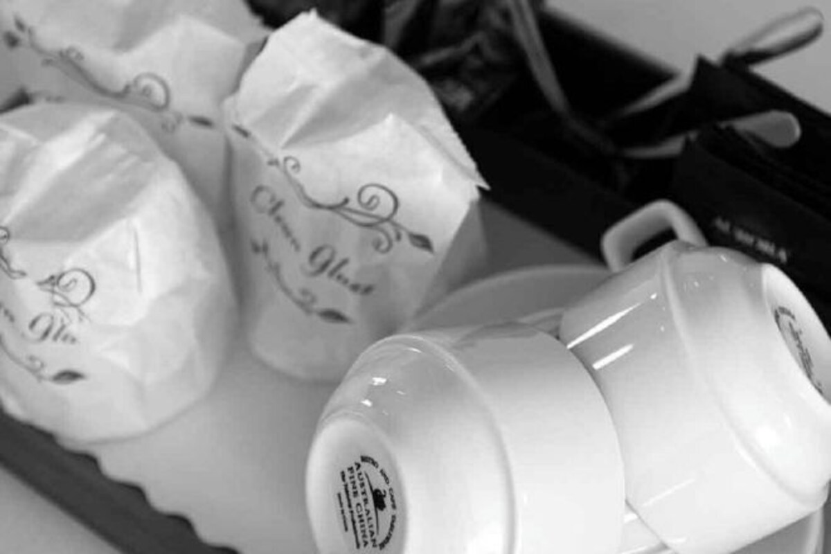 Primer plano de una taza de cerámica blanca con una etiqueta, rodeada de bolsas de papel arrugadas con texto.
