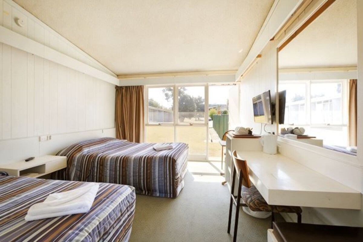 A motel room with two beds, a desk, a chair, a TV, and a window with a view of the outside.