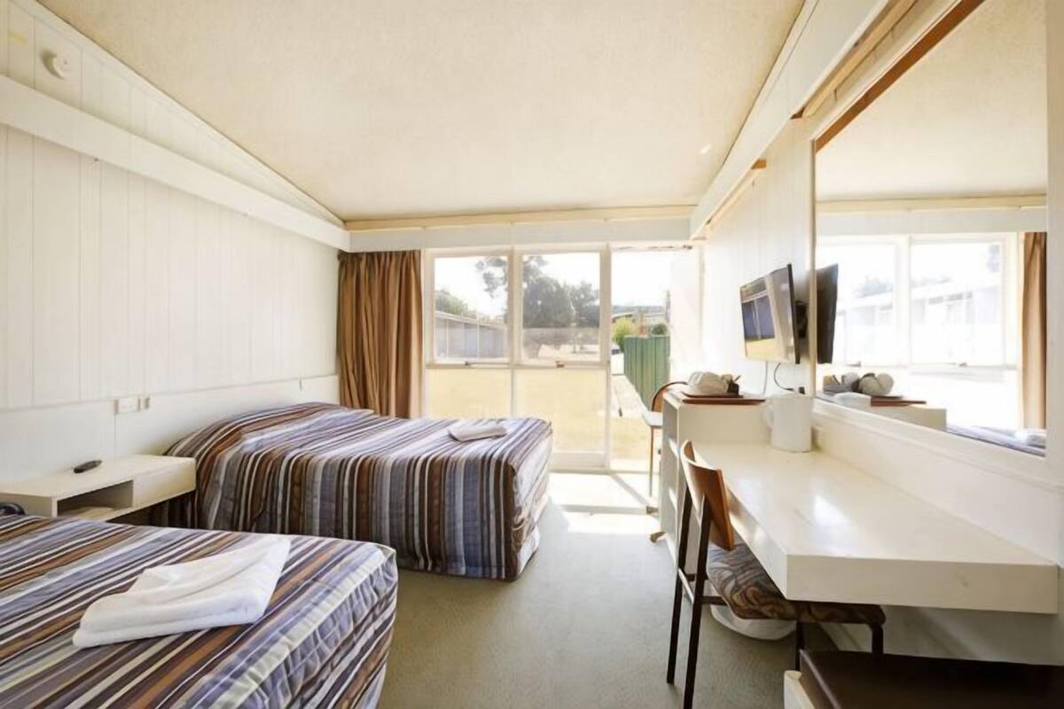 A motel room with two beds, a desk, a chair, a TV, and a window with a view of the outside.