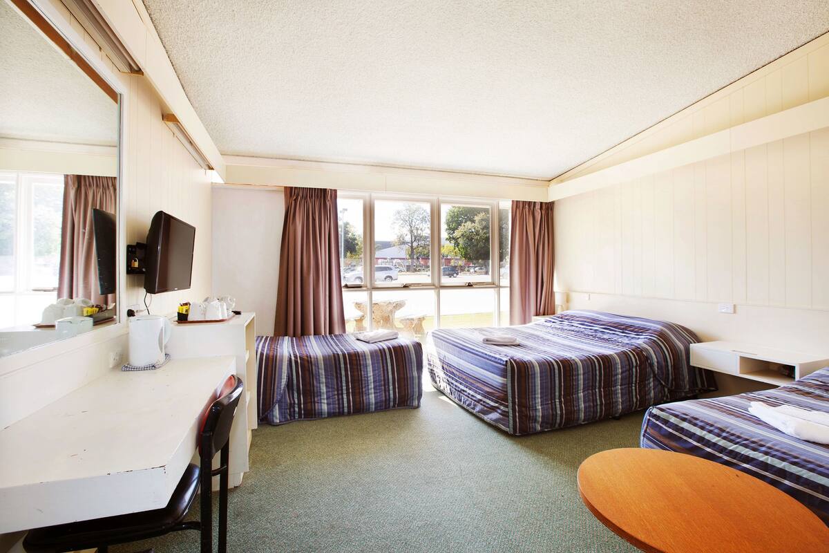 A hotel room with two beds, a desk, a chair, a small table, and a television.