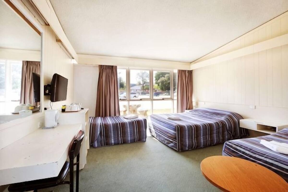 A hotel room with two beds, a desk, a chair, a television, and a window with curtains.