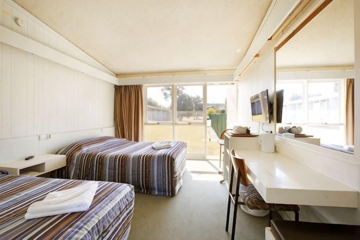 A motel room with two beds, a desk, a chair, a TV, and a window with a view of the outside.