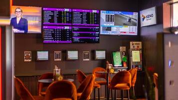 A hotel lobby with multiple screens displaying information, a seating area with chairs, and a KENO gaming machine.