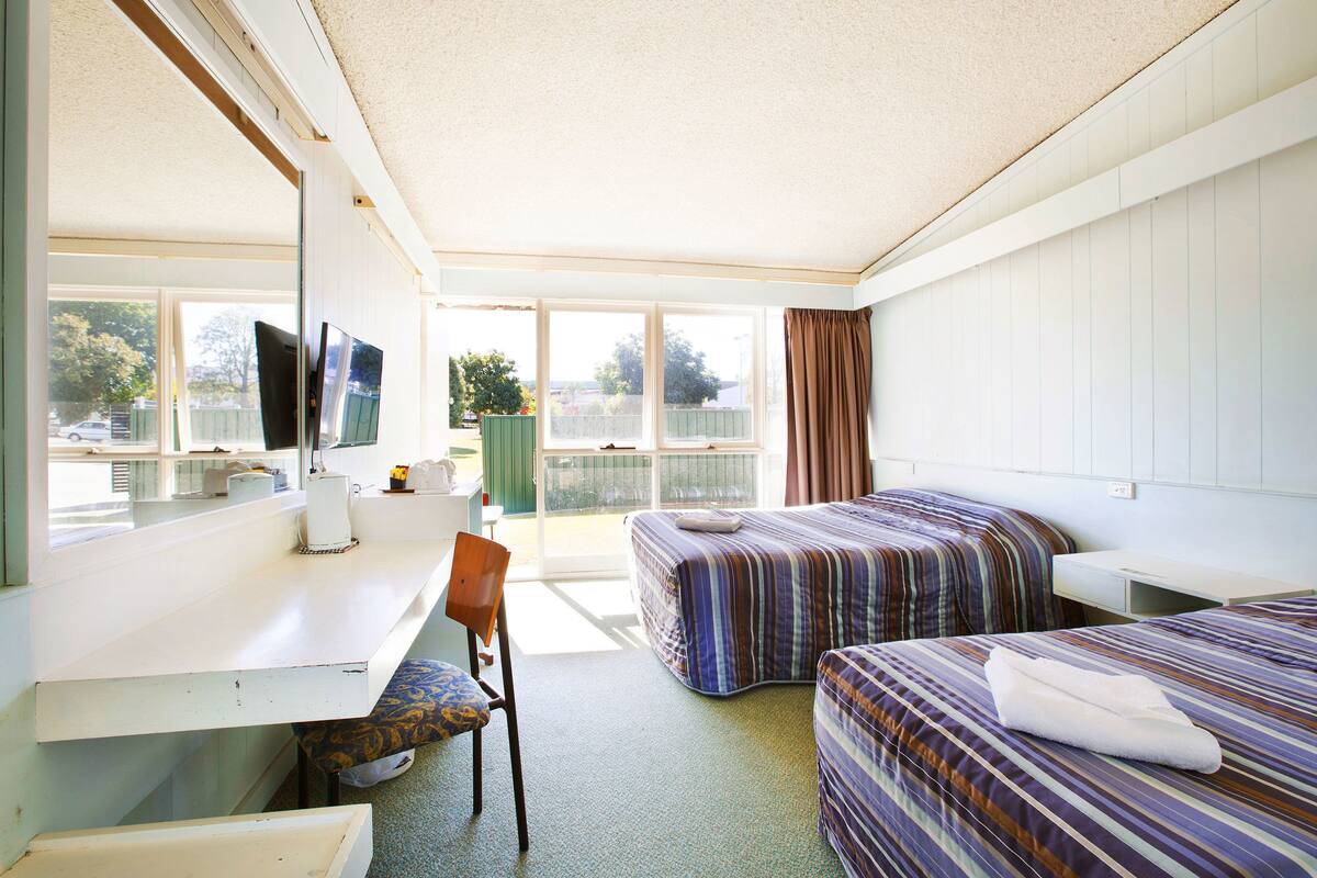 A hotel room with a desk, two beds, a chair, and a TV.