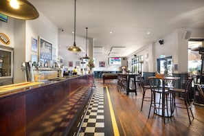 A bar area with a checkered floor, wooden bar counter, and multiple hanging pendant lights. - Nightcap at Wanneroo Tavern (Wanneroo)