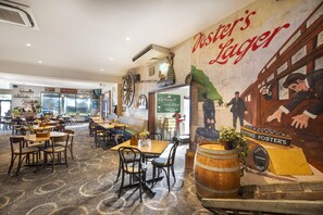 A restaurant with tables and chairs, a mural on the wall, and a sign for Foster's Lager.