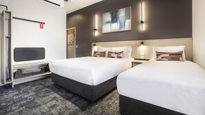 Une chambre d’hôtel avec deux lits, un bureau, une chaise, une armoire et un grand tableau abstrait accroché au mur.