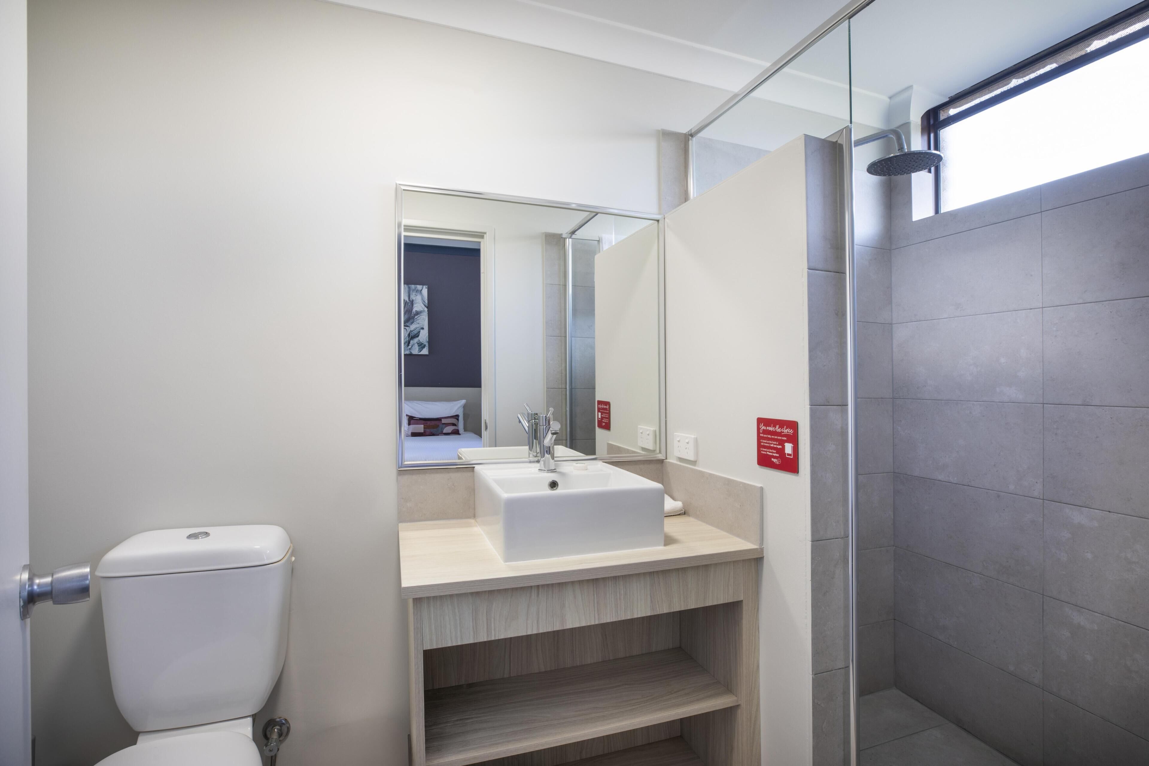 A modern bathroom with a white toilet, a sink with a mirror, and a shower area.