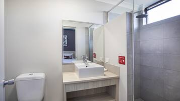 Un baño moderno con inodoro blanco, lavamanos con espejo y cabina de ducha.