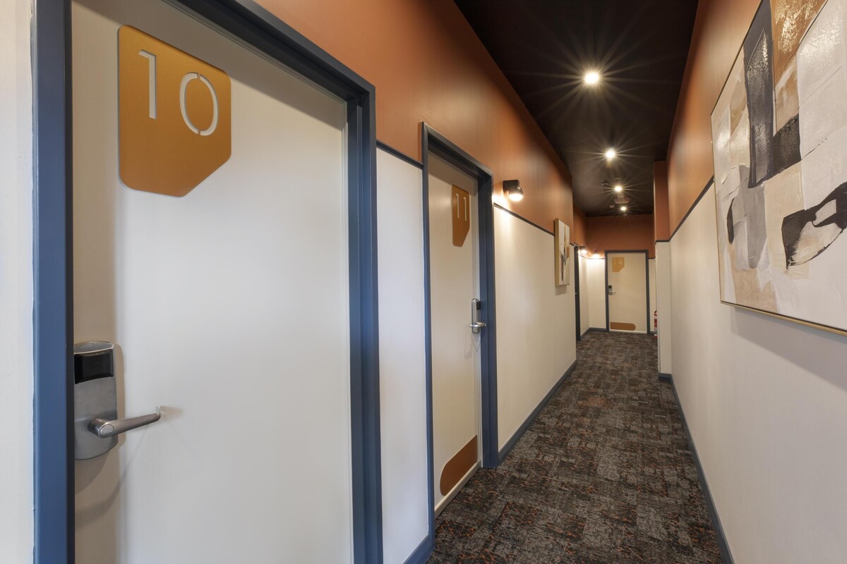 A hallway with doors marked with numbers, carpeted flooring, and recessed lighting.