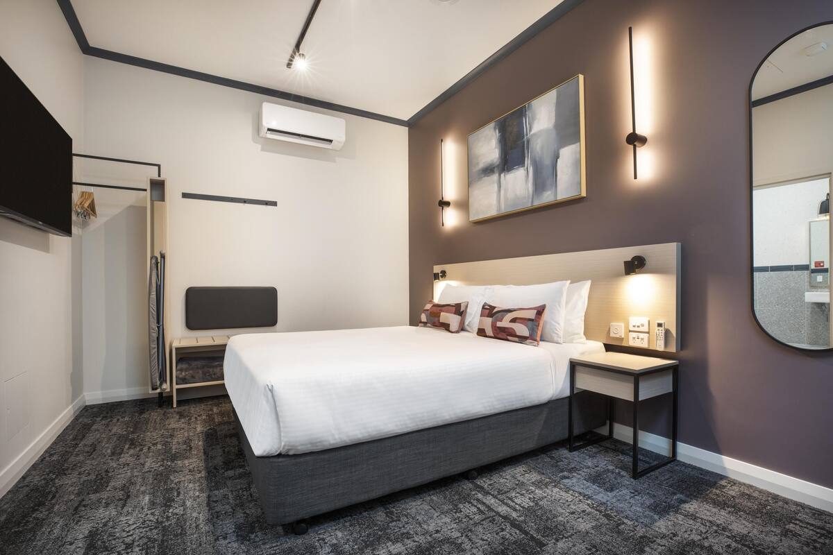 A modern hotel room with a large bed, bedside table, wall-mounted artwork, and a mirror.