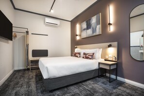 Una habitación de hotel moderna con una cama grande, mesita de noche, obra de arte en la pared y un espejo.