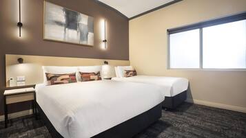 A hotel room with two beds, a desk, a chair, a large window, and a painting on the wall.