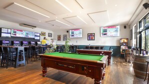 Une salle de billard équipée de plusieurs tables de billard, d’un bar et de plusieurs écrans diffusant des informations.