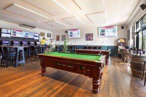 Una sala biliardo con diversi tavoli da biliardo, un'area bar e vari schermi che mostrano informazioni.