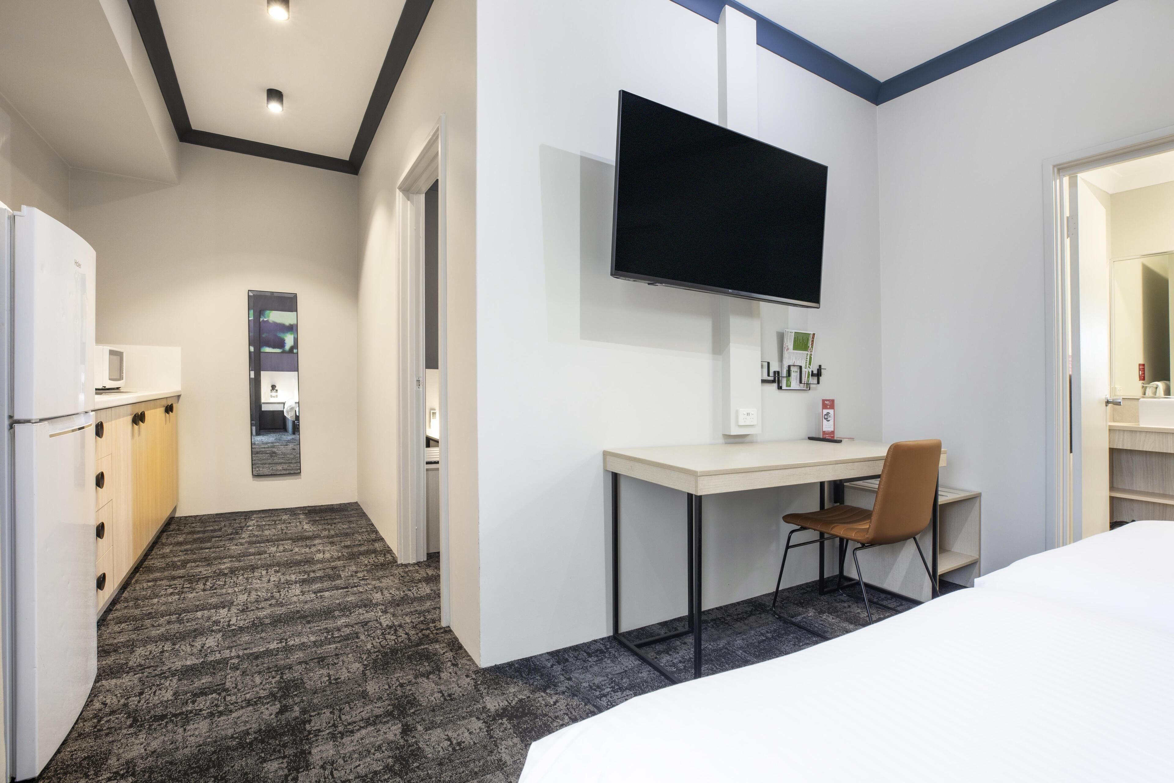 Habitación de hotel con cama, escritorio con silla, televisión de pantalla plana, minibar y una pequeña kitchenette.