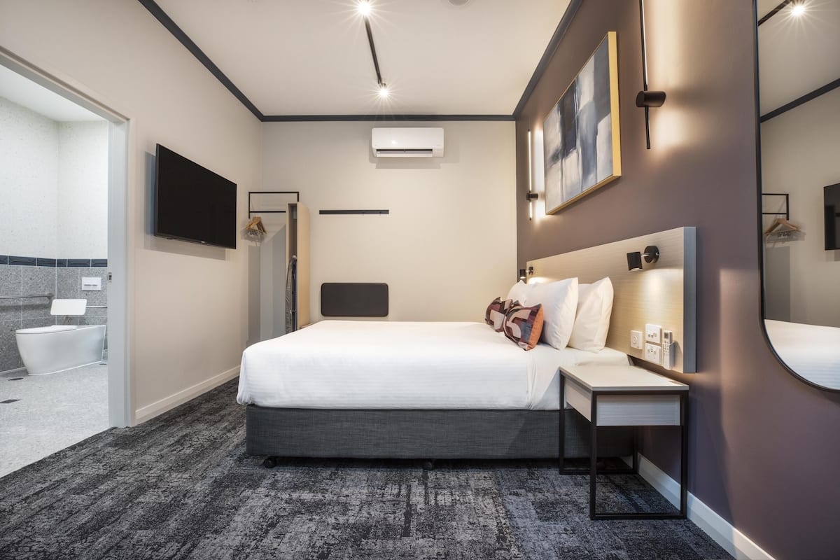 A modern hotel room with a large bed, bedside table, and a flat-screen TV.