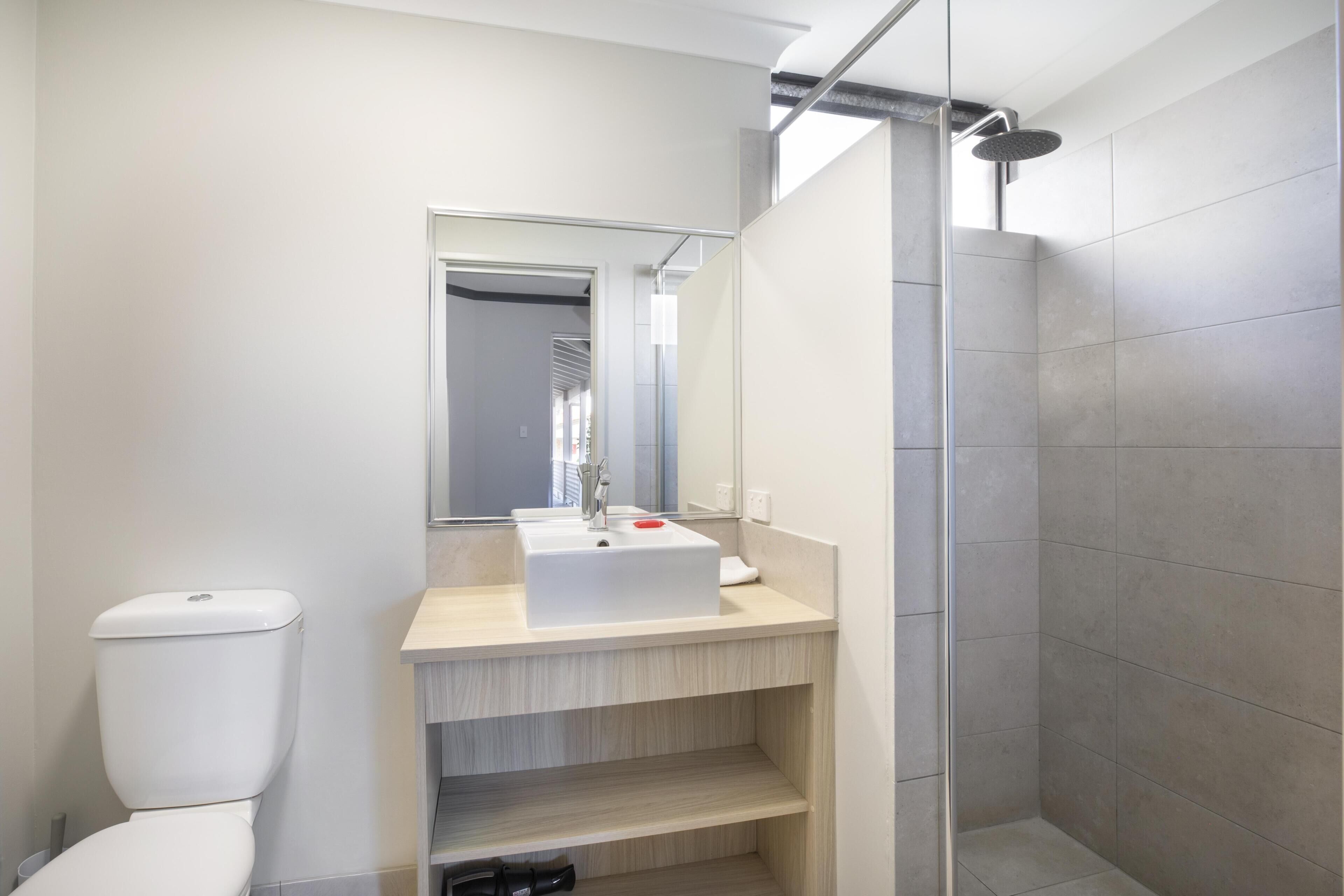 Un baño moderno con inodoro, lavamanos, espejo y ducha.