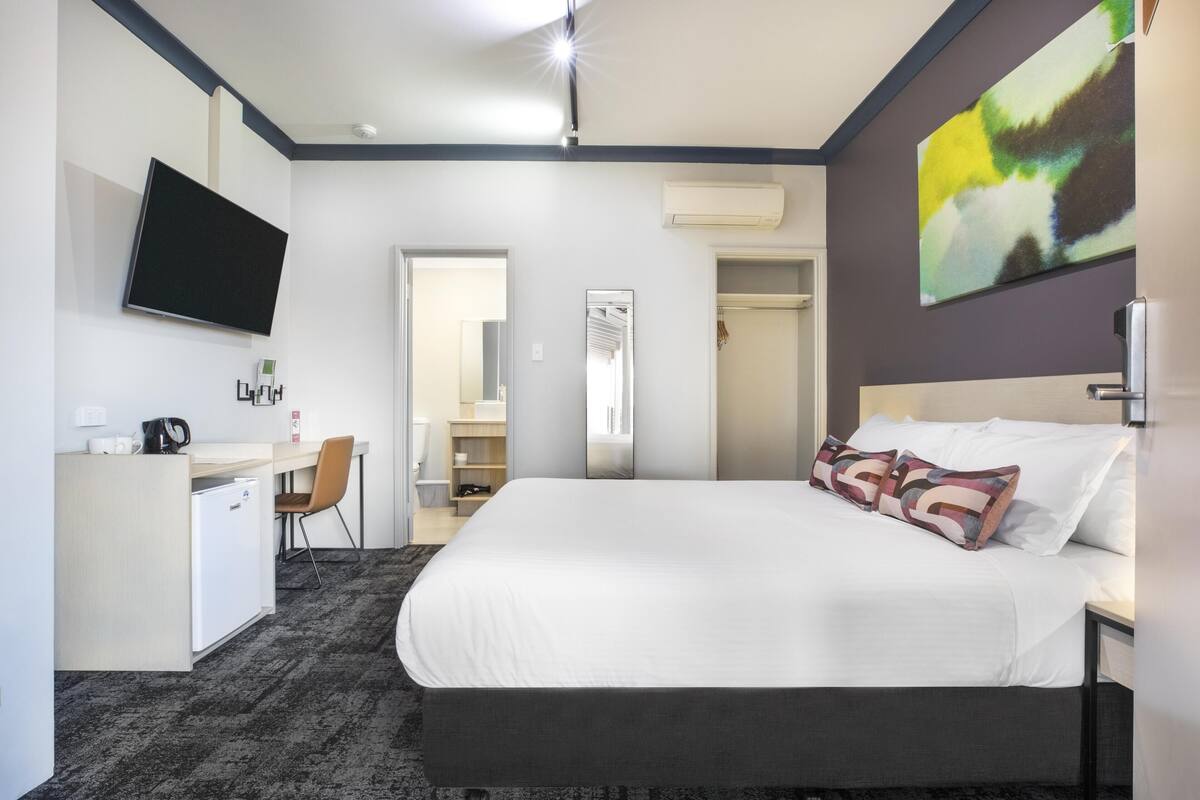 A hotel room with a bed, a desk, a chair, a television, and a bathroom door.