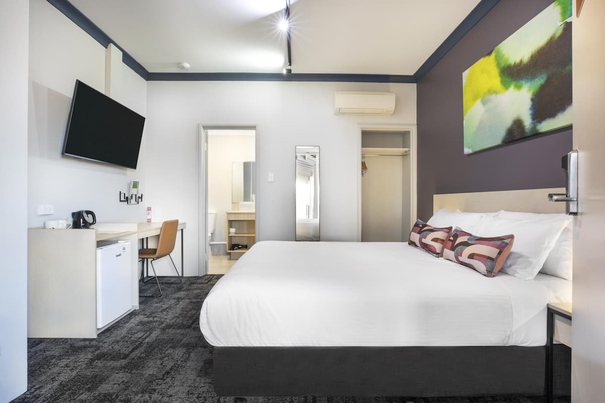 Une chambre d’hôtel avec un lit, un bureau, une chaise, une télévision et une porte de salle de bain.