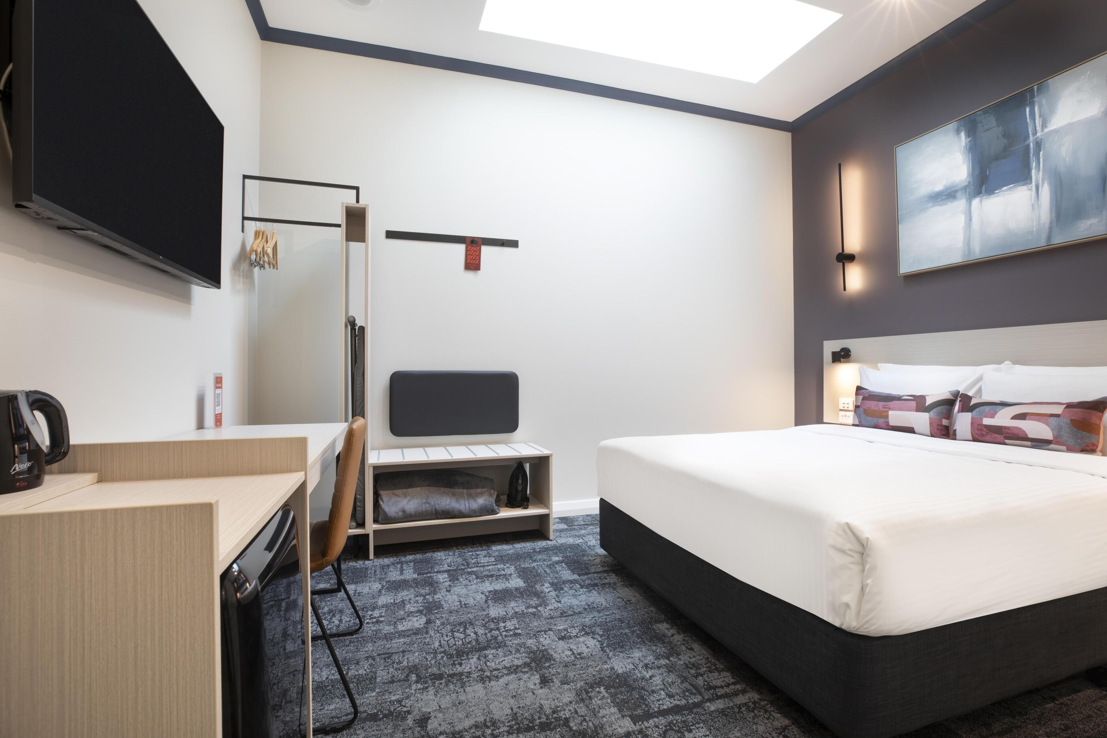 Una habitación de hotel con cama, escritorio, silla y televisor montado en la pared.
