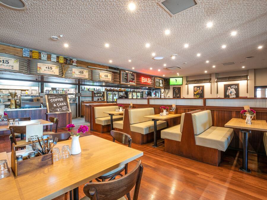 Un restaurant avec des banquettes et des tables, un coin bar et un tableau affichant le menu.