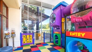Un espace de jeux intérieur coloré, avec un sol à carreaux, un toboggan violet et une structure de jeu portant l’inscription « ENTRÉE ».