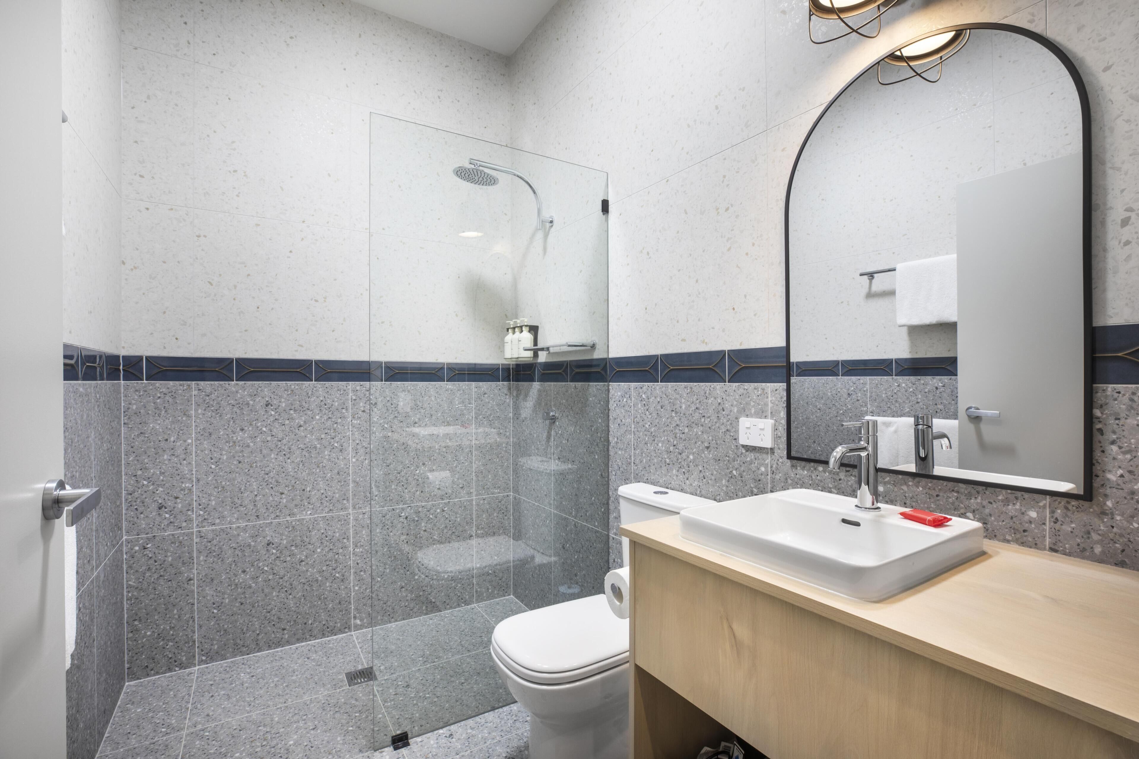 A modern bathroom with a shower, toilet, sink, and mirror.