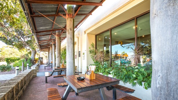 Une terrasse ext érieure avec des tables et des bancs en bois, entourée de verdure et dotée d’une allée couverte.