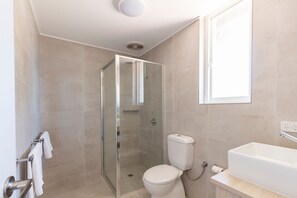 A modern bathroom with a glass shower enclosure, a white toilet, and a large bathtub.