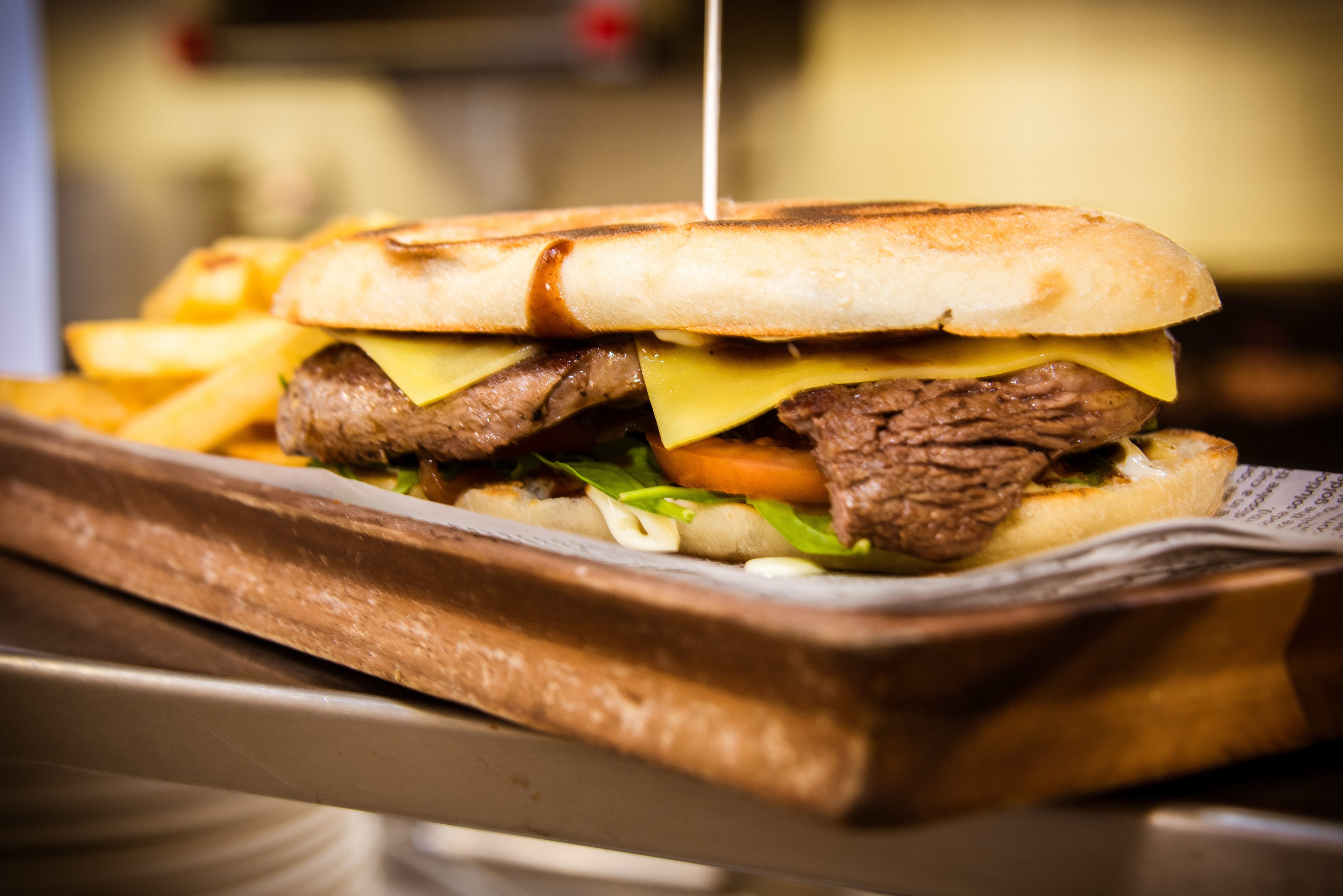 A sandwich with a toasted bun, beef, cheese, lettuce, and tomato, served on a tray.