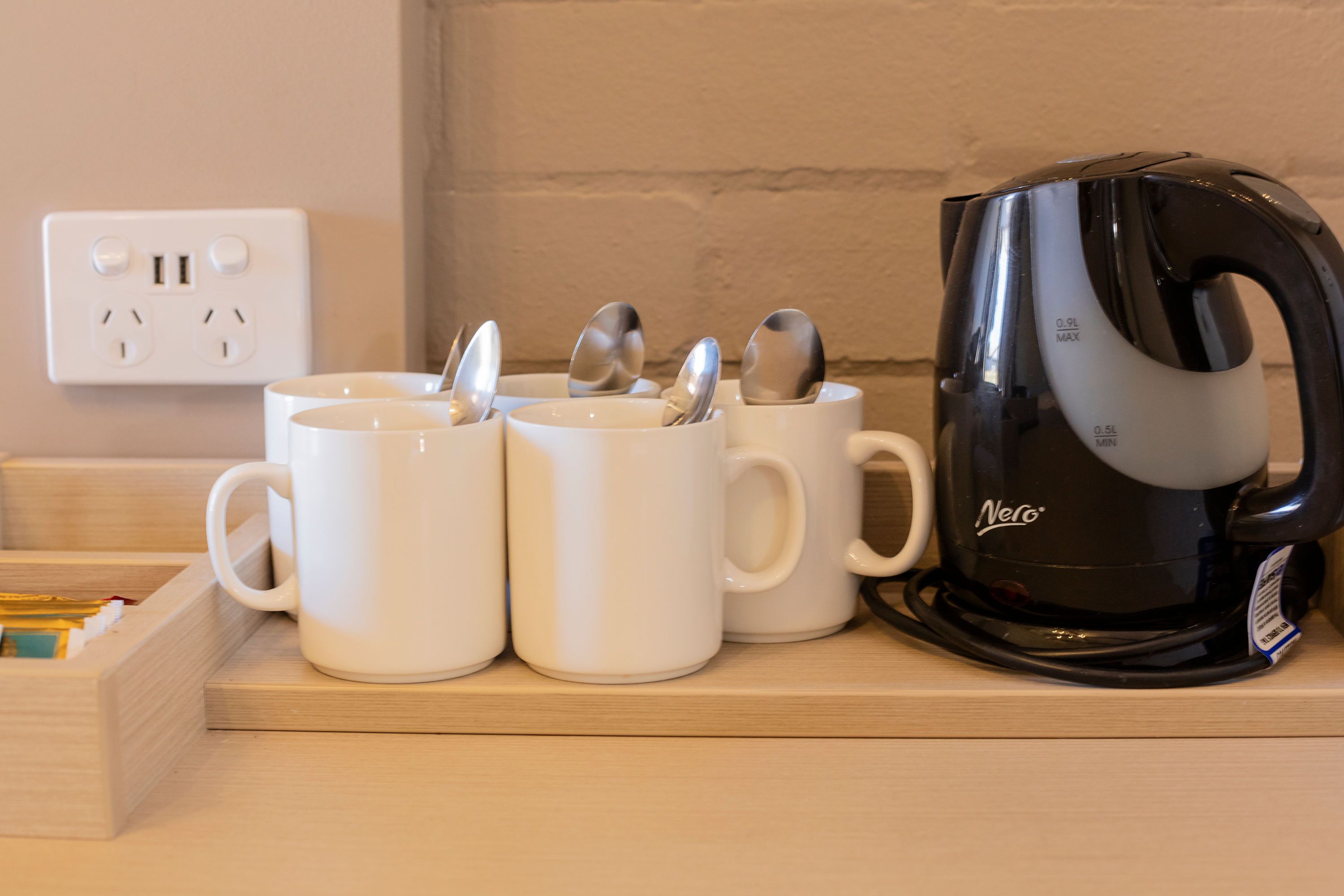 A kitchen counter with white mugs, spoons, and a black coffee maker.