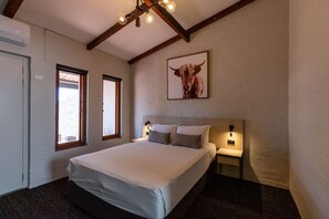 A bedroom with a large bed, two bedside tables, a wall-mounted light, and a window with a view.