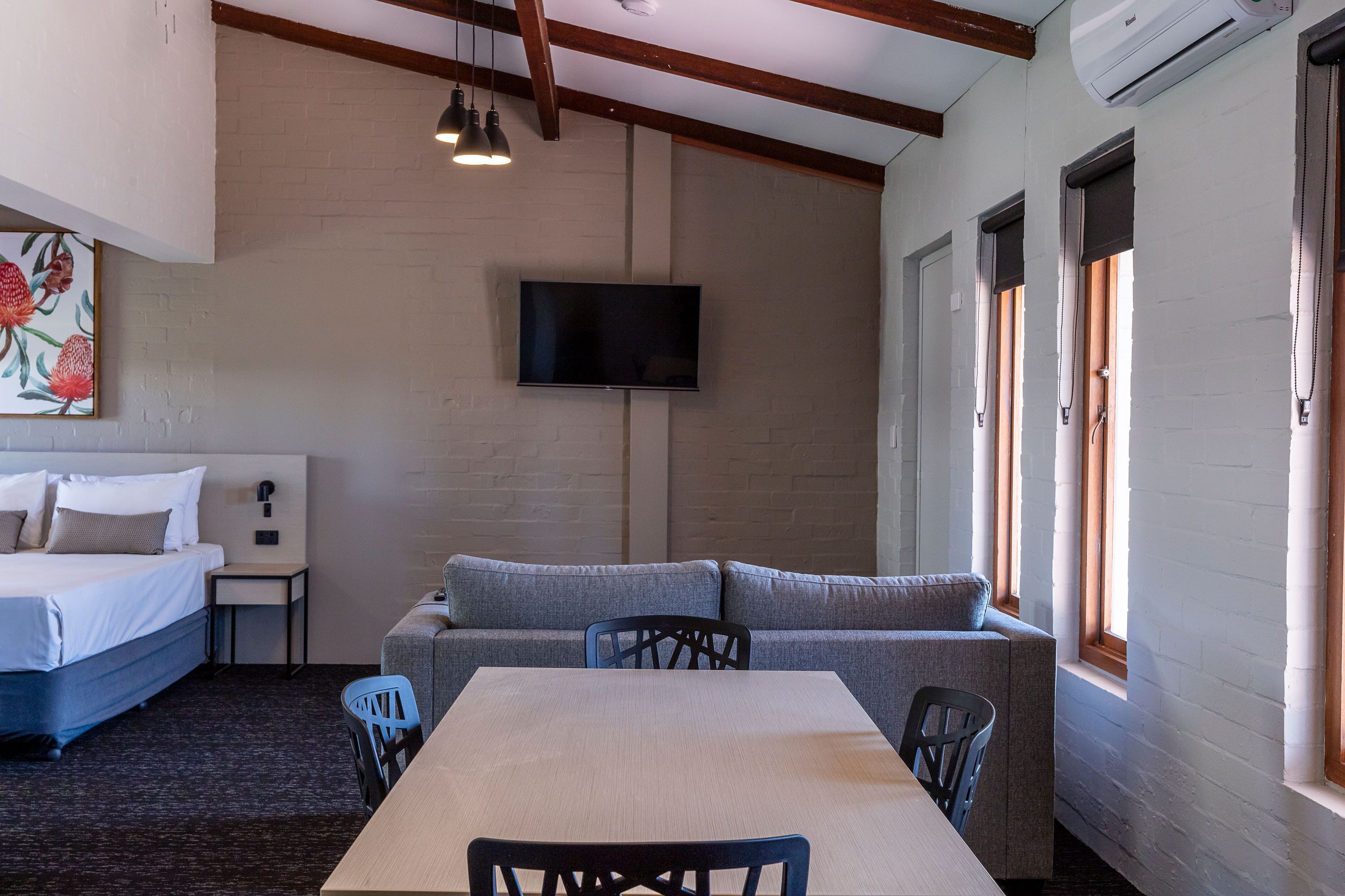 A hotel room with a bed, a sofa, a dining table, and a TV mounted on the wall.