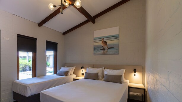 Hotelkamer met twee enkele bedden, een groot bed, een schilderij van een kangoeroe en een plafondlamp.