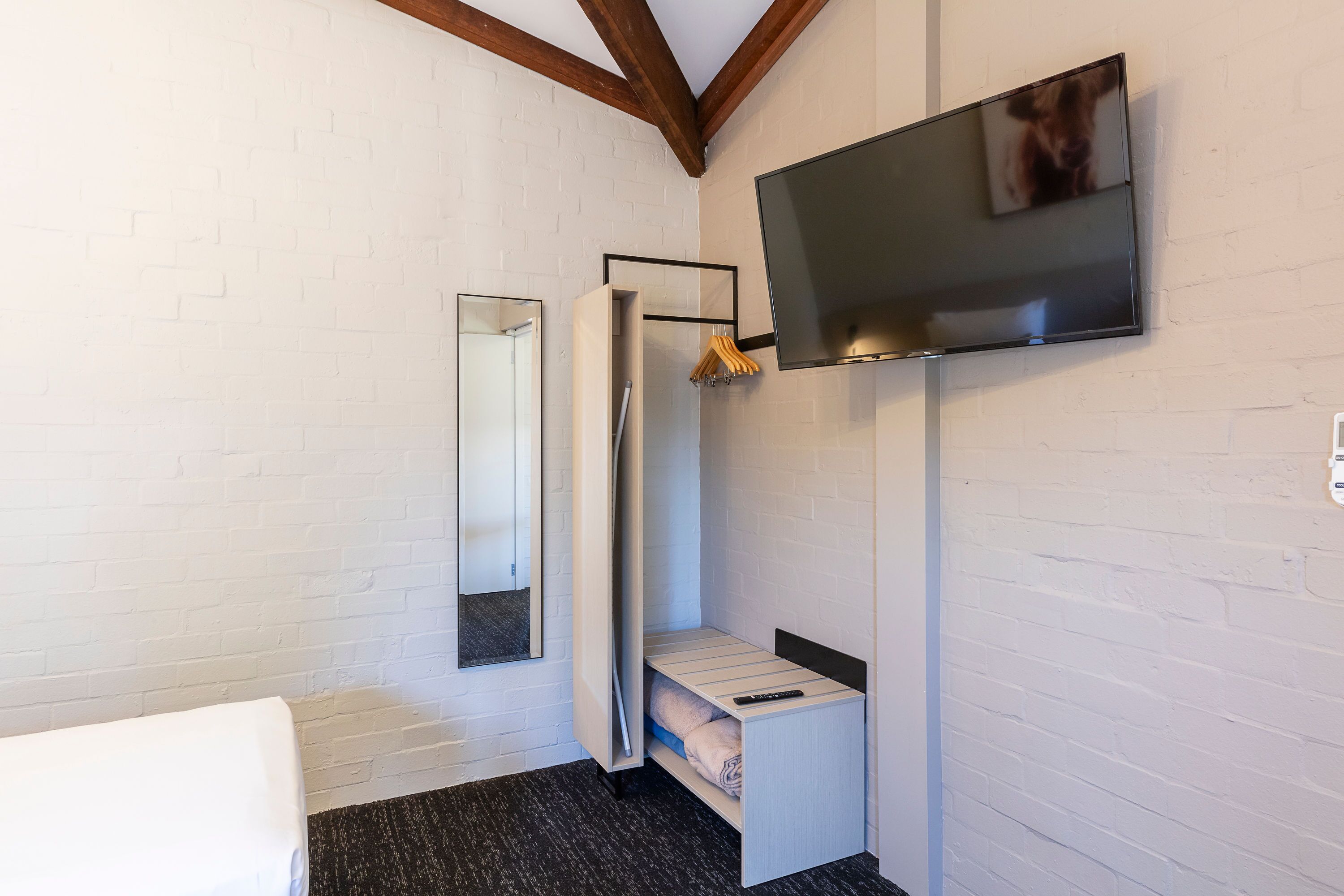 A compact room with a bed, a TV, a mirror, and a small storage unit.
